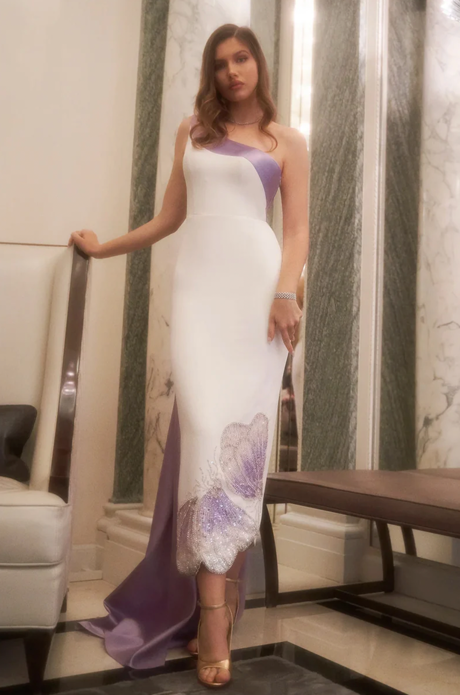 Indulge in modern romance with the Iris Gown. This two-tone masterpiece of heavy satin and crepe showcases a column silhouette with a soft, scalloped hem and exquisite hand-embroidered beadwork in a delicate wing design. Finished with a trailing swathe of fabric at the back, this gown is sure to make a statement.