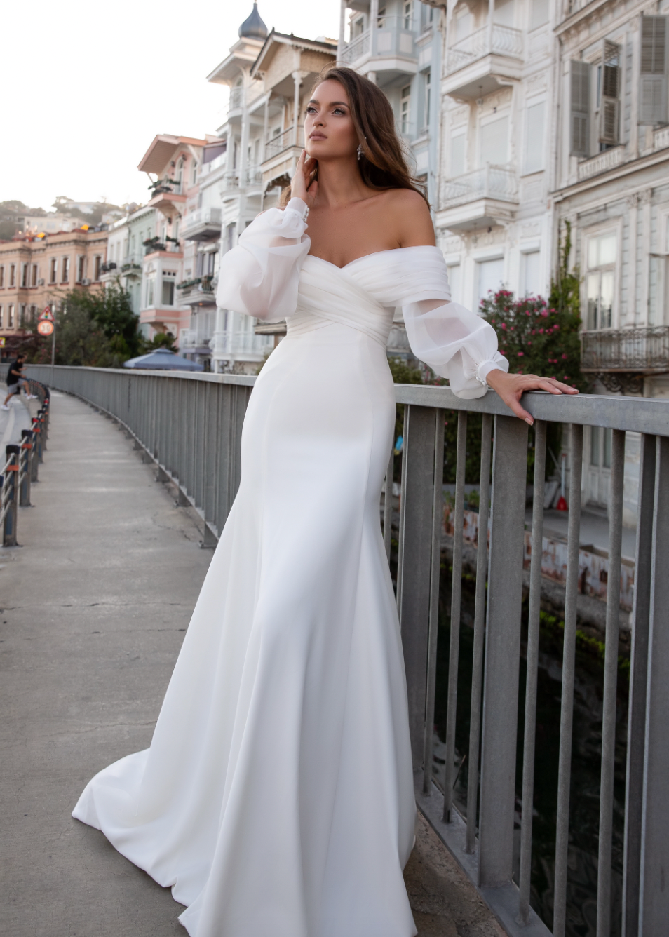 Experience pure elegance with Robe Alora! This bohemian-inspired wedding dress features a sexy satin mermaid silhouette, long lace sleeves, and sultry off-the-shoulder detailing for a ravishing and timeless look. Get ready to turn heads on your special day!