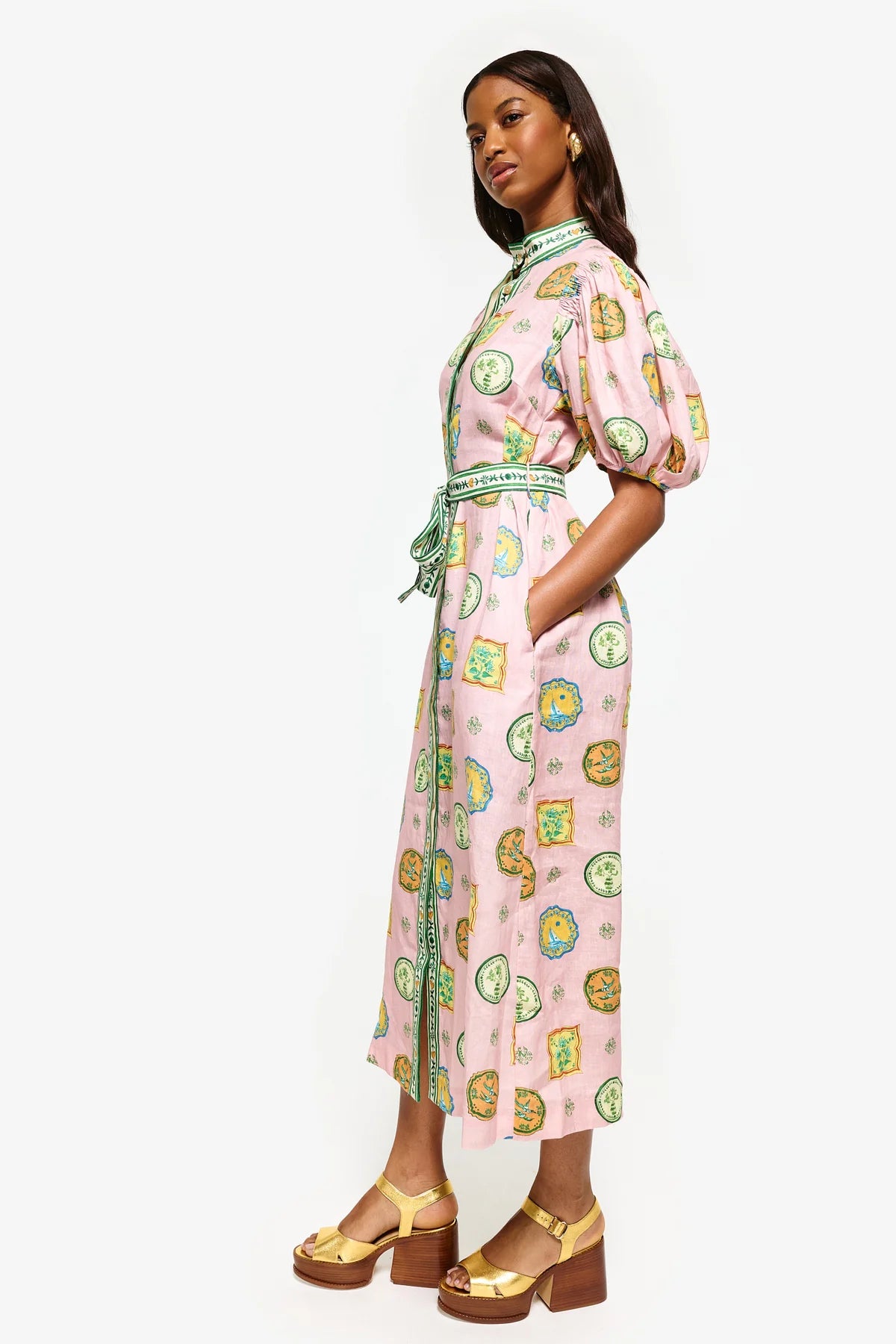 Get ready to turn heads at your next summer dinner party with the Porcelain Shirtdress! This delightful pink midi features charming green and yellow accents and a fitted silhouette with elasticated balloon sleeves. The elegant shell buttons, in-seam pockets, and self-tie belt add practicality and playful details. Elevate your summer style with the Porcelain Shirtdress.