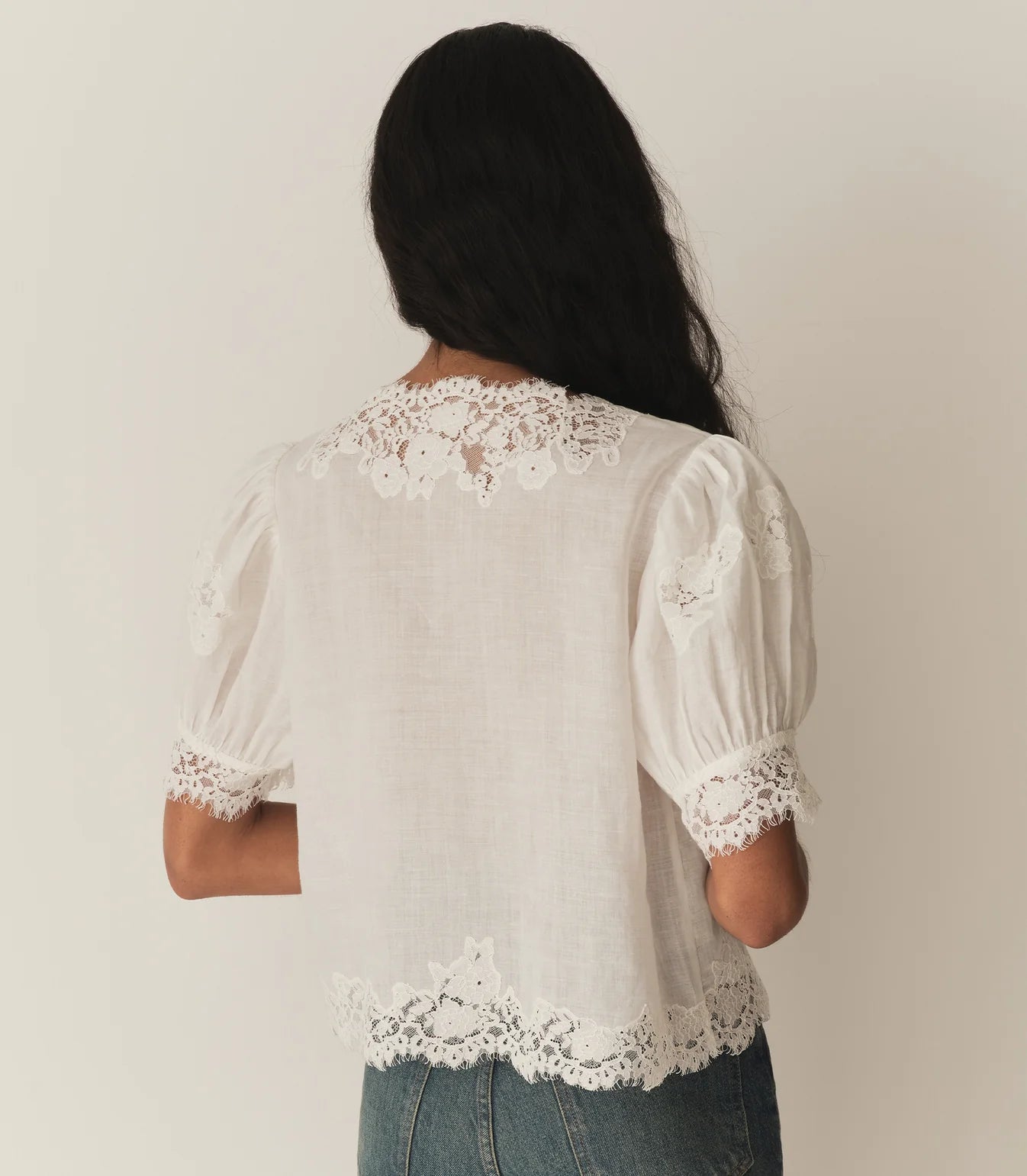 Crafted from lightweight, crisp ramie, the Idella Top from Doen features a plunging V-neckline, short puffed sleeves, and intricate embroidered lace details. Mother-of-pearl buttons adorn the front, while lace insets add delicate touches. This antique-inspired top is perfect for a breezy, feminine look.