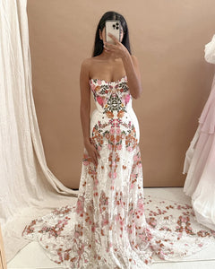 Introducing Meadow Gown - a work of art inspired by desert blooms. Its vibrant florals are delicately embroidered on sand-dyed tulle, creating a stunning contrast against bare terrain. With a fully boned bodice for support and a dramatic train with cascading flowers, this gown exudes a playful yet sophisticated charm. Perfect for the bold bride looking to infuse color into her special day.