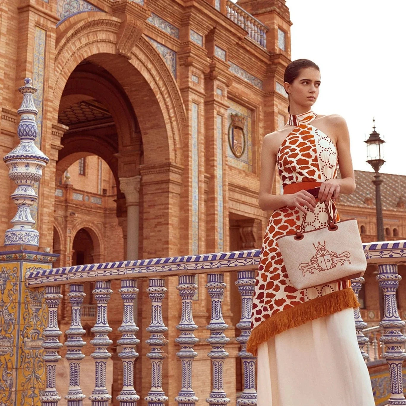 The Eliane Dress is a flowy, long dress with a halter neckline. The ruffled top of the skirt and fringe detailing add a playful touch. It features a sleeveless design and hidden back zipper for a seamless look. The vibrant orange and beige print will make you stand out in any occasion.