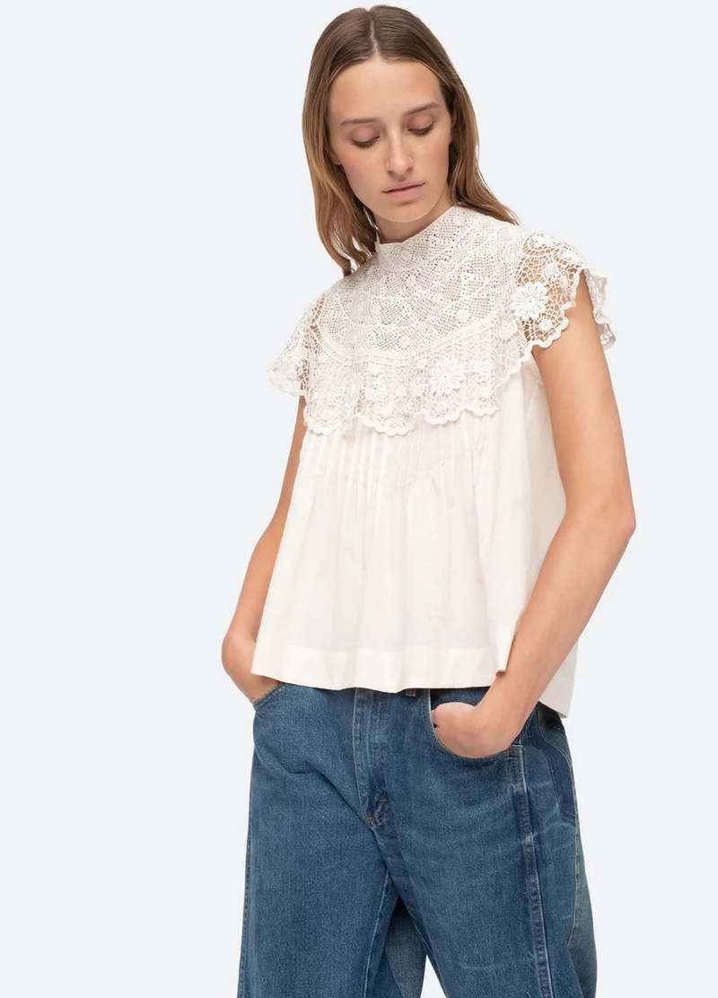 Be a vision of delicate beauty in the Serita Top by Sea New York. This cream-colored top boasts a crochet lace cape and intricate stitched pleat detailing, creating a whimsical and feminine look. The perfect addition to any wardrobe for adding a touch of elegance and charm.