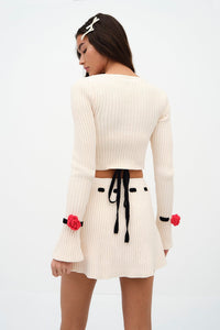 Indulge in luxury with the Roxana Cardigan by For Love & Lemons. Made of a midweight chenille ribbed knit fabric, this cropped cardigan features a round neck and front snap button closure adorned with delicate rosette appliques. The long sleeves and removable chenille rosette on the cuffs add a touch of elegance to this unlined piece. Available in a timeless white color, this cardigan is perfect for adding a touch of sophistication to any outfit.