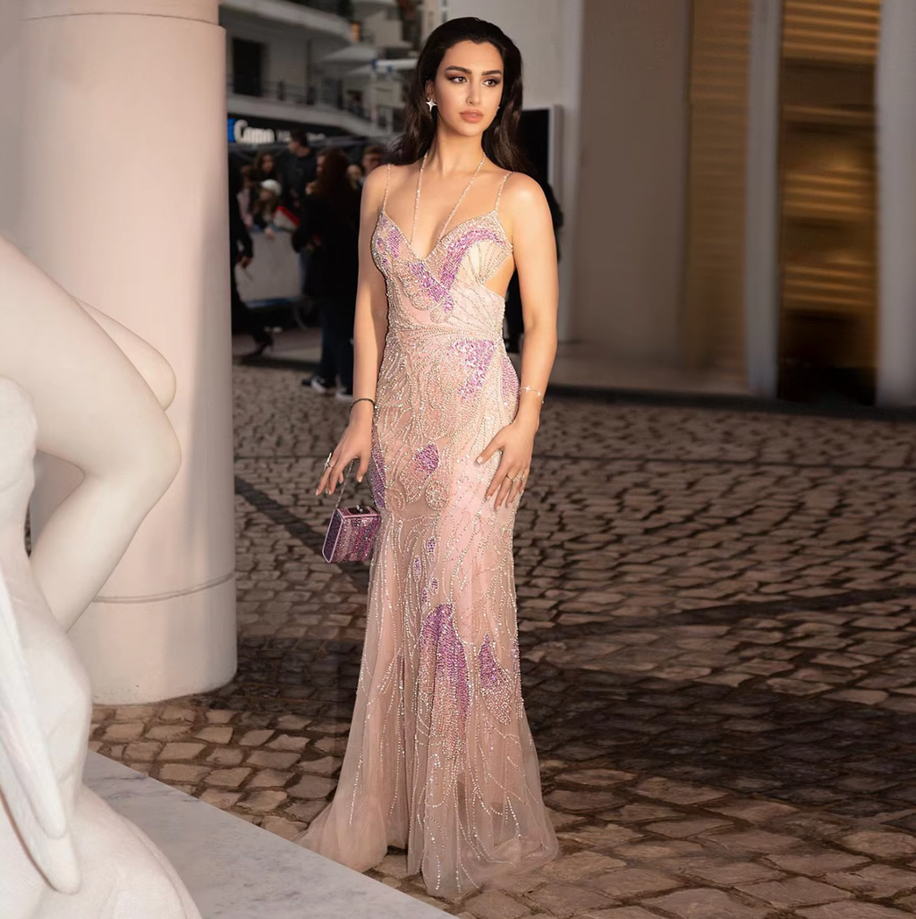 The Bardot Gown is a luxurious evening dress with a mermaid-style silhouette, featuring elegant rose-colored straps and a delicate feather scarf. Perfect for formal events and weddings, this gown is customizable and inspired by the glamorous fashion of Dubai.