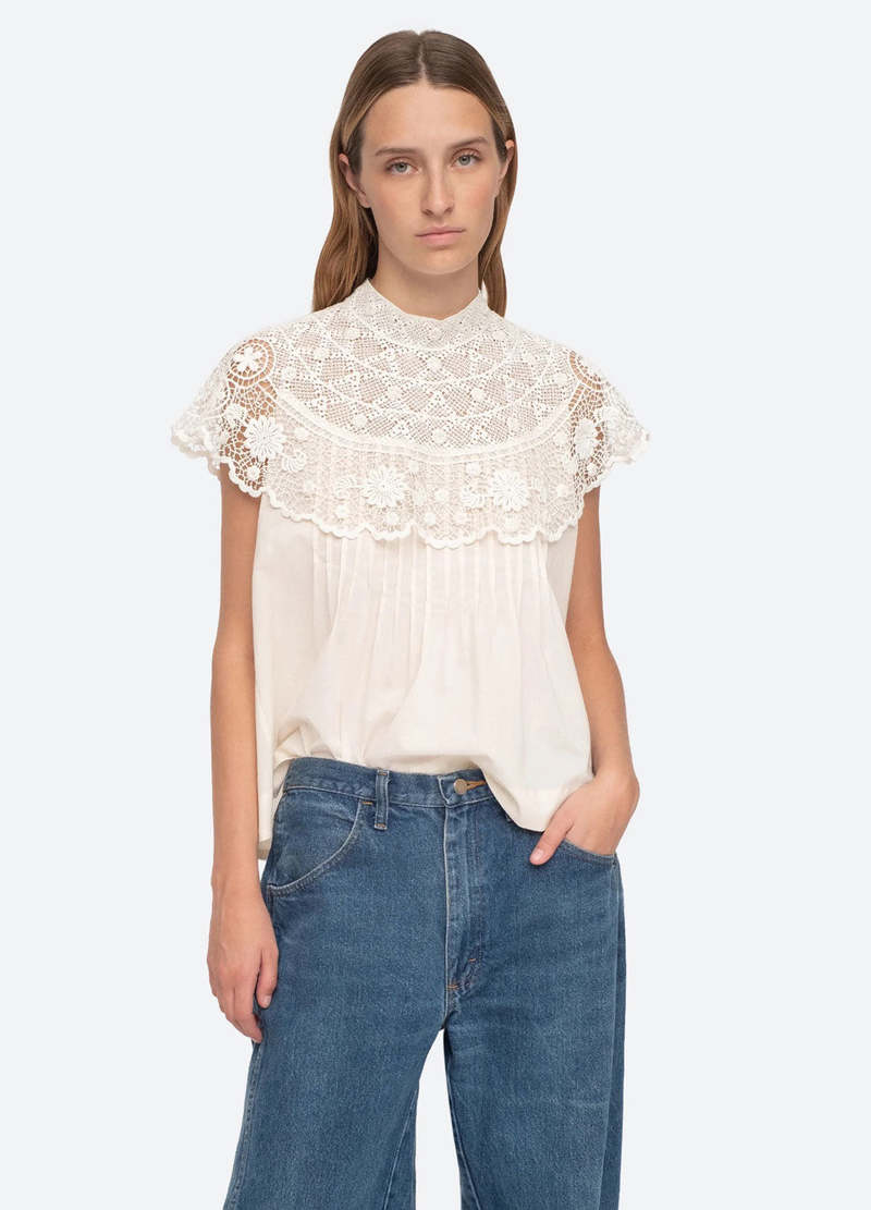 Be a vision of delicate beauty in the Serita Top by Sea New York. This cream-colored top boasts a crochet lace cape and intricate stitched pleat detailing, creating a whimsical and feminine look. The perfect addition to any wardrobe for adding a touch of elegance and charm.