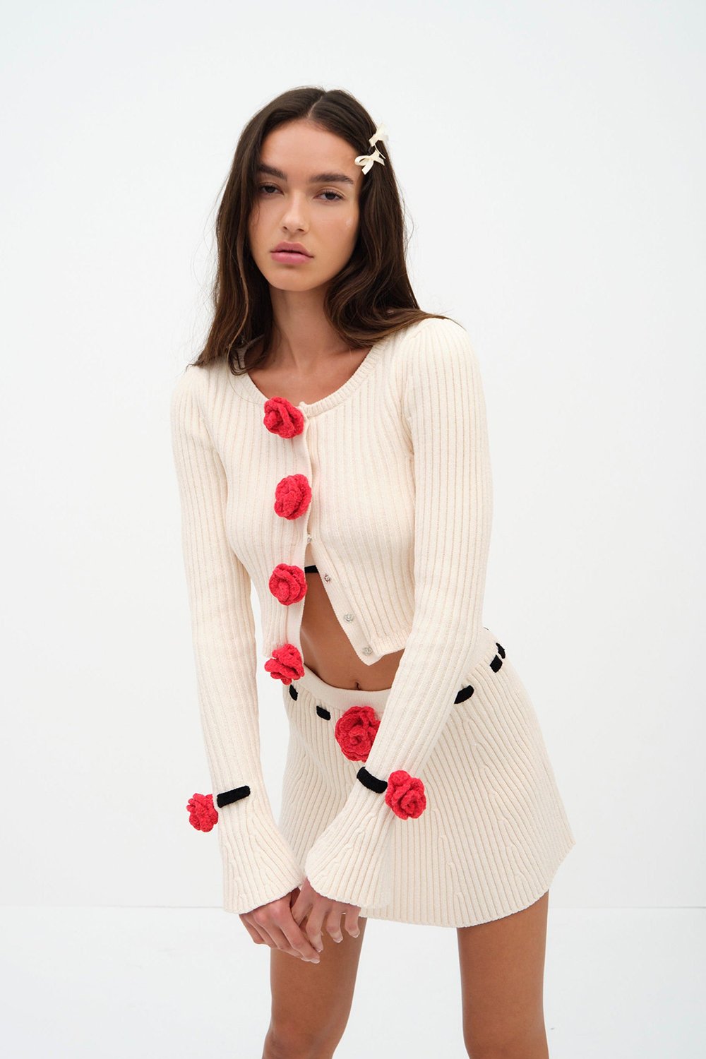 Indulge in luxury with the Roxana Cardigan by For Love & Lemons. Made of a midweight chenille ribbed knit fabric, this cropped cardigan features a round neck and front snap button closure adorned with delicate rosette appliques. The long sleeves and removable chenille rosette on the cuffs add a touch of elegance to this unlined piece. Available in a timeless white color, this cardigan is perfect for adding a touch of sophistication to any outfit.