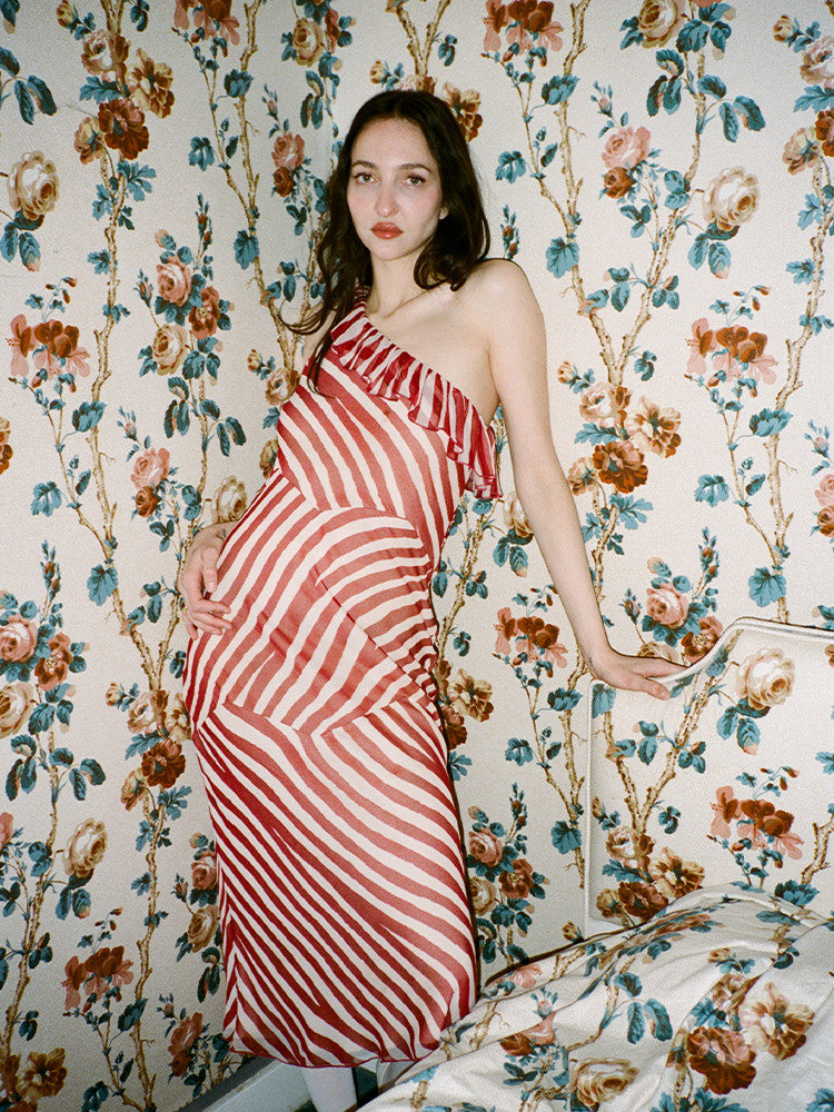 Indulge in the timeless charm of Theodora Maxi Dress. Its one-shouldered design and silk candy stripes evoke a sense of theatrical elegance. Panelled seams create an abstract stripe pattern in cream and deep red hues. Cinch the waist for added allure and pair with a dark lip and pointed heels for a touch of old-school Parisian chic.