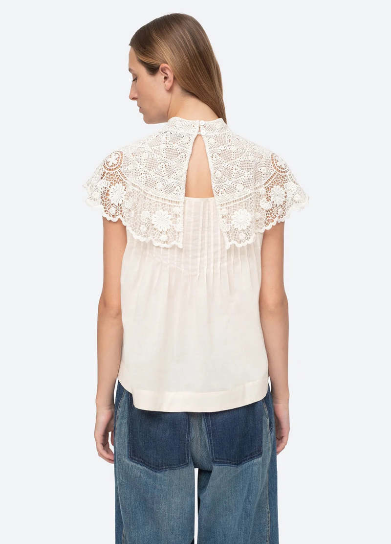 Be a vision of delicate beauty in the Serita Top by Sea New York. This cream-colored top boasts a crochet lace cape and intricate stitched pleat detailing, creating a whimsical and feminine look. The perfect addition to any wardrobe for adding a touch of elegance and charm.