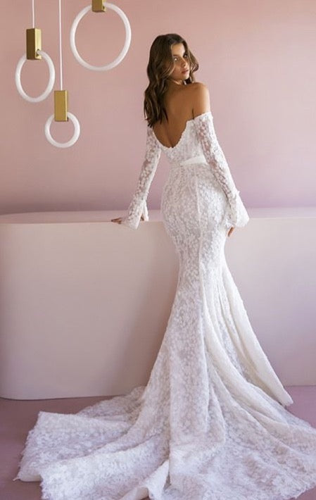 Indulge in the timeless elegance of the Robe Jeane. This strapless column showcases bare shoulders and long sleeves, adorned with delicate applique flowers. The exquisite lace flows into a dazzling train, while a white silk ribbon cinches the waist. Experience luxury with beaded accents and a delicate row of buttons down the back.