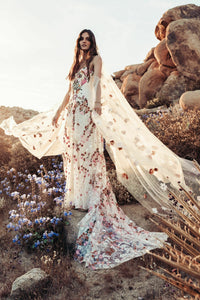 Introducing Meadow Gown - a work of art inspired by desert blooms. Its vibrant florals are delicately embroidered on sand-dyed tulle, creating a stunning contrast against bare terrain. With a fully boned bodice for support and a dramatic train with cascading flowers, this gown exudes a playful yet sophisticated charm. Perfect for the bold bride looking to infuse color into her special day.