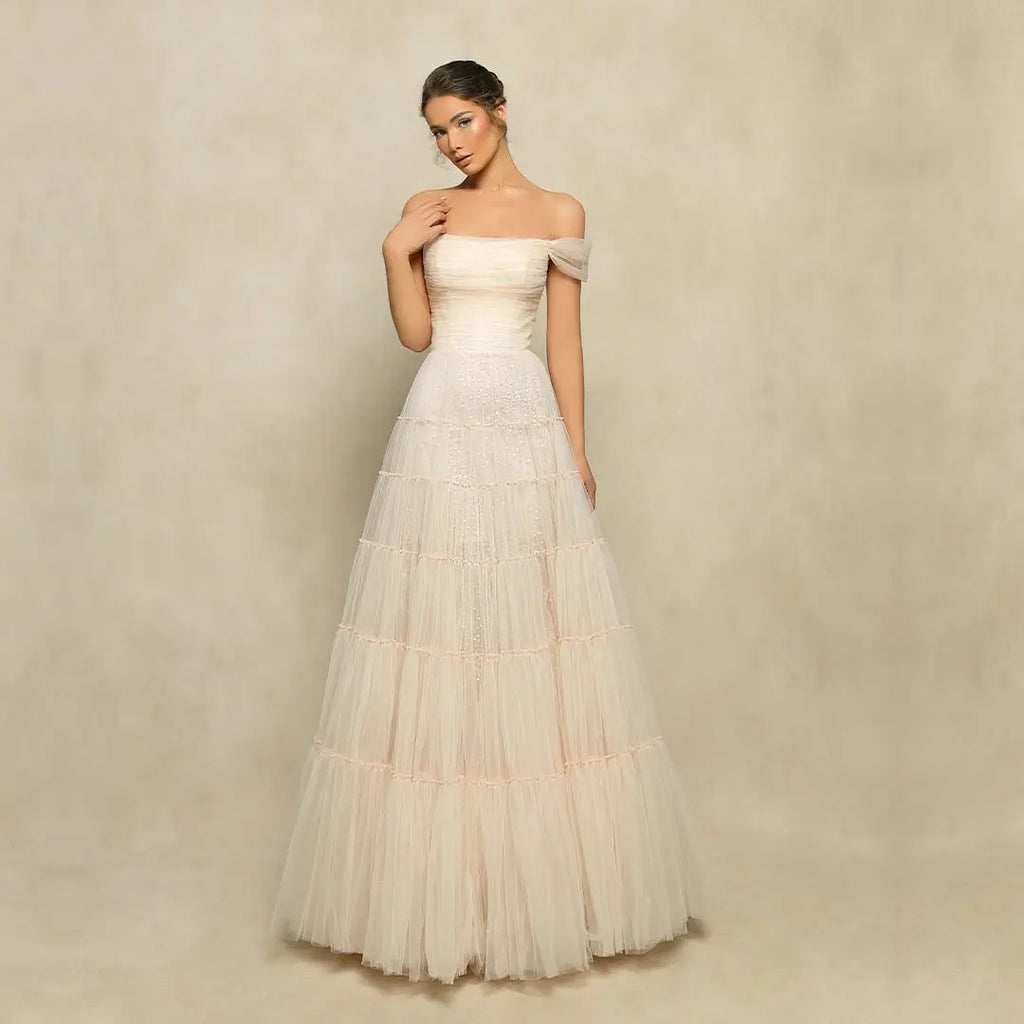 Unleash your inner charm with the Amina Gown. This stunning evening gown features a tiered A-line skirt with a tulle overlay adorned with delicate beadwork, adding a touch of subtle shimmer. The structured bodice boasts a sheer, ruched off-shoulder neckline, creating an elegant and radiant look. Dare to be bold in this captivating creation.