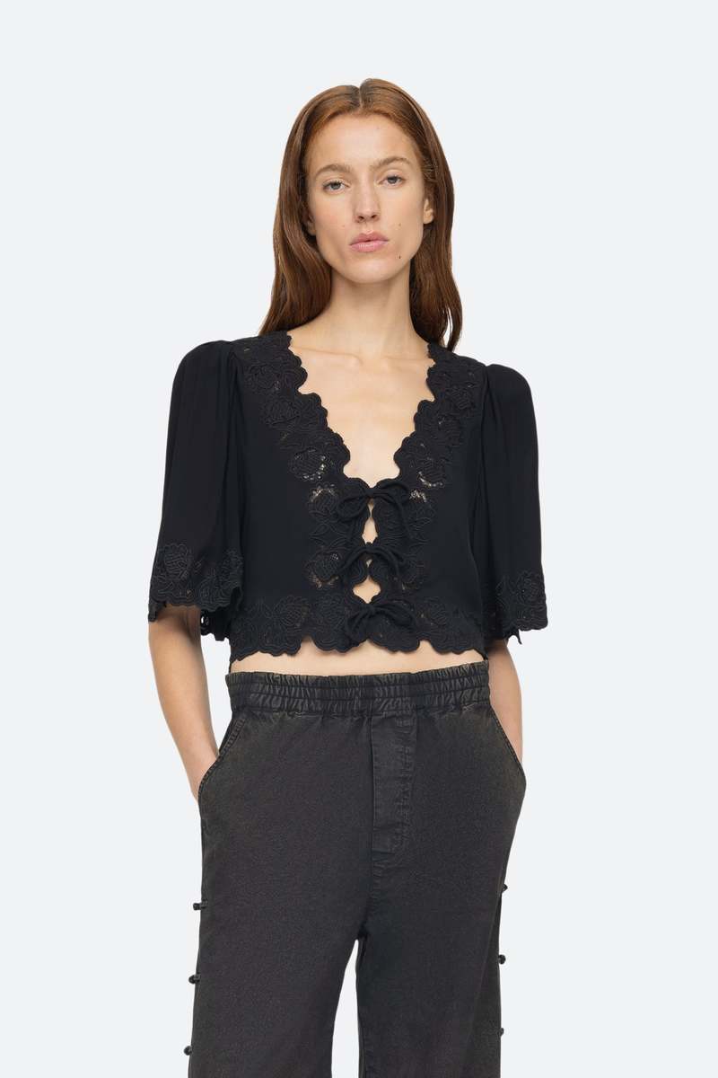 Elevate your wardrobe with the effortlessly elegant Baylin Top in Black by SEA. Delicate lace detailing and front tie closures exude sophistication and charm, while the flowy short sleeves add a touch of femininity. Luxurious and versatile, this top is a must-have for any occasion.