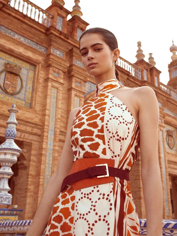 The Eliane Dress is a flowy, long dress with a halter neckline. The ruffled top of the skirt and fringe detailing add a playful touch. It features a sleeveless design and hidden back zipper for a seamless look. The vibrant orange and beige print will make you stand out in any occasion.