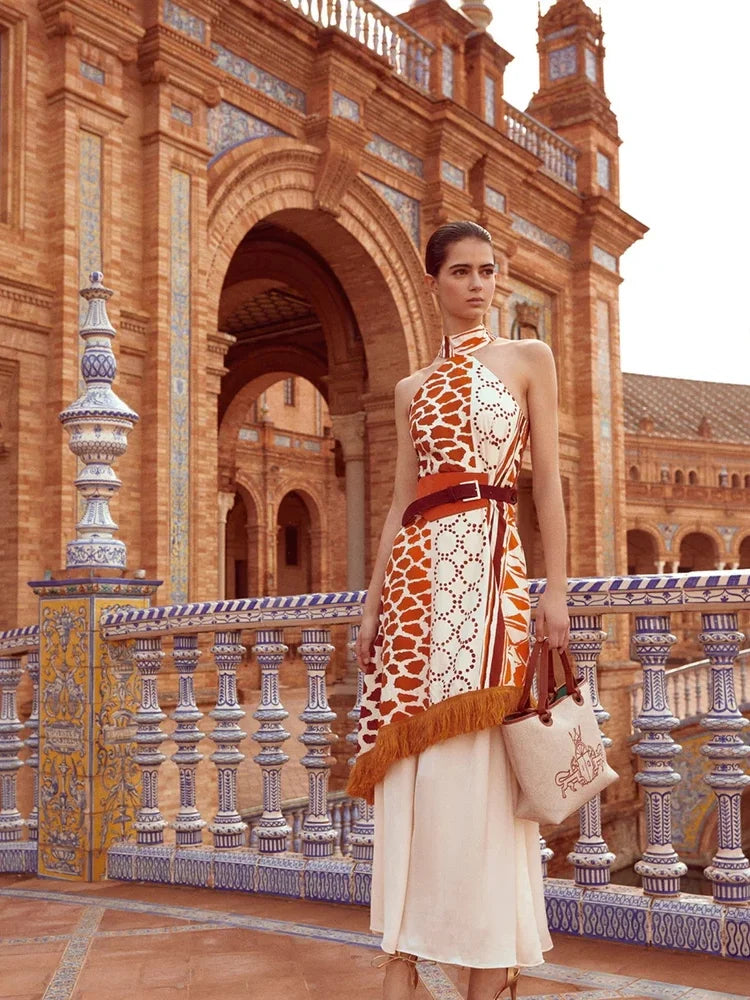 The Eliane Dress is a flowy, long dress with a halter neckline. The ruffled top of the skirt and fringe detailing add a playful touch. It features a sleeveless design and hidden back zipper for a seamless look. The vibrant orange and beige print will make you stand out in any occasion.