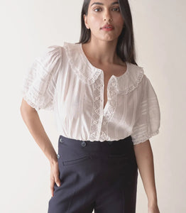 In the softest organic cotton voile, the Bernadine Top by Doen offers a blend of vintage charm and contemporary flair. Featuring a Peter Pan collar and short puffed sleeves adorned with pintucks and inset lace, this slightly cropped blouse is detailed with mother-of-pearl buttons down the front. Delicate scallop-edged butterfly lace trims the collar and sleeve cuffs, enhancing its feminine appeal. Perfect for adding a touch of elegance to any casual ensemble.