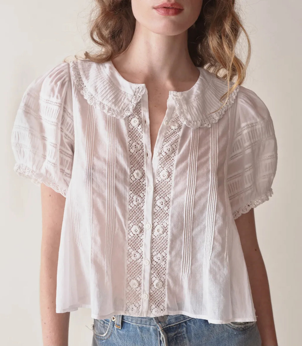 In the softest organic cotton voile, the Bernadine Top by Doen offers a blend of vintage charm and contemporary flair. Featuring a Peter Pan collar and short puffed sleeves adorned with pintucks and inset lace, this slightly cropped blouse is detailed with mother-of-pearl buttons down the front. Delicate scallop-edged butterfly lace trims the collar and sleeve cuffs, enhancing its feminine appeal. Perfect for adding a touch of elegance to any casual ensemble.