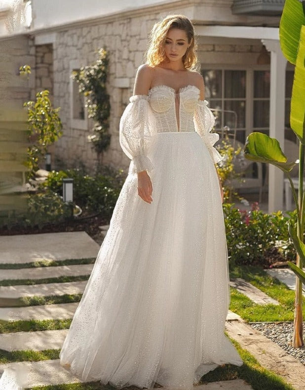 Get ready to turn heads in the Robe Alara! With its off-shoulder, sweetheart neckline and A-line silhouette, this bohemian wedding dress is both chic and comfortable. The delicate lace and long sleeves add an extra touch of romance, while the buttons down the back and floor-length skirt create a stunning finishing touch. Say yes to style and comfort on your special day!