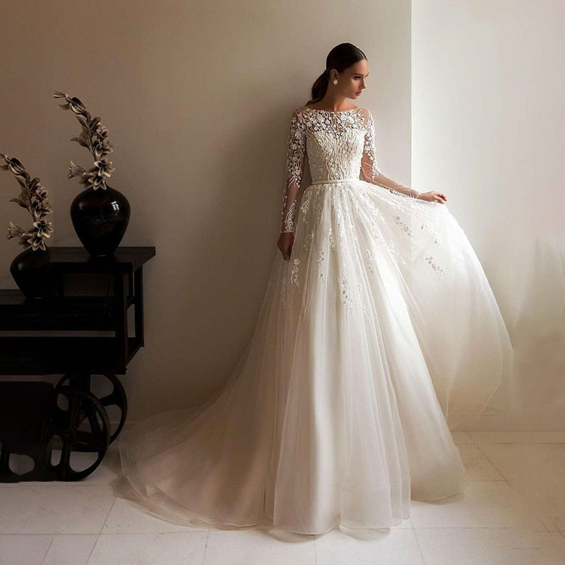 Elevate your wedding look with the Robe Anneliese. This A-line wedding dress features elegant illusion lace long-sleeves and a scoop neckline for a timeless and sophisticated look. The applique tulle train adds a touch of romance and sophistication. Make a statement on your special day in this beautiful bridal gown.