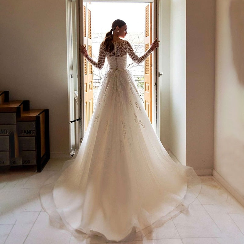 Elevate your wedding look with the Robe Anneliese. This A-line wedding dress features elegant illusion lace long-sleeves and a scoop neckline for a timeless and sophisticated look. The applique tulle train adds a touch of romance and sophistication. Make a statement on your special day in this beautiful bridal gown.