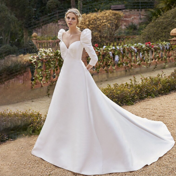 The Robe Cerys is a stunning satin wedding dress with a v-neckline, puffed sleeves, and a dramatic train. Designed for plus-size brides, it features elegant buttons and a flattering cut that will make you feel confident and beautiful on your special day. With a perfect balance of glamour and comfort, this dress is sure to make a lasting impression.