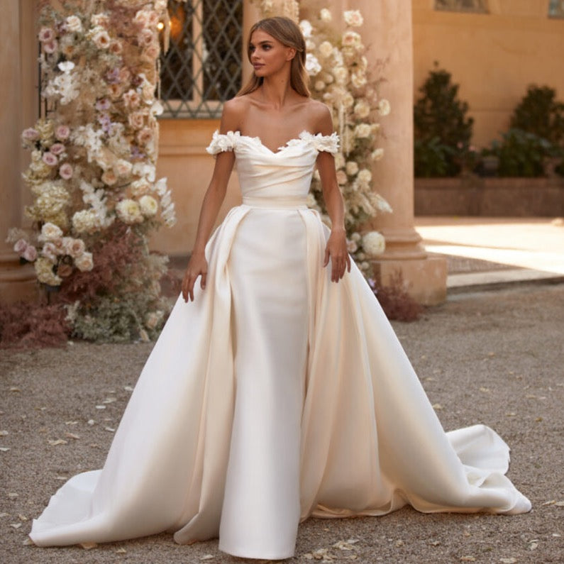 Robe Rachela is a stunning bridal gown with off-shoulder neckline and detachable train for a versatile look. Its figure-hugging silhouette and siren-style shape guarantee to make a statement for your special night.