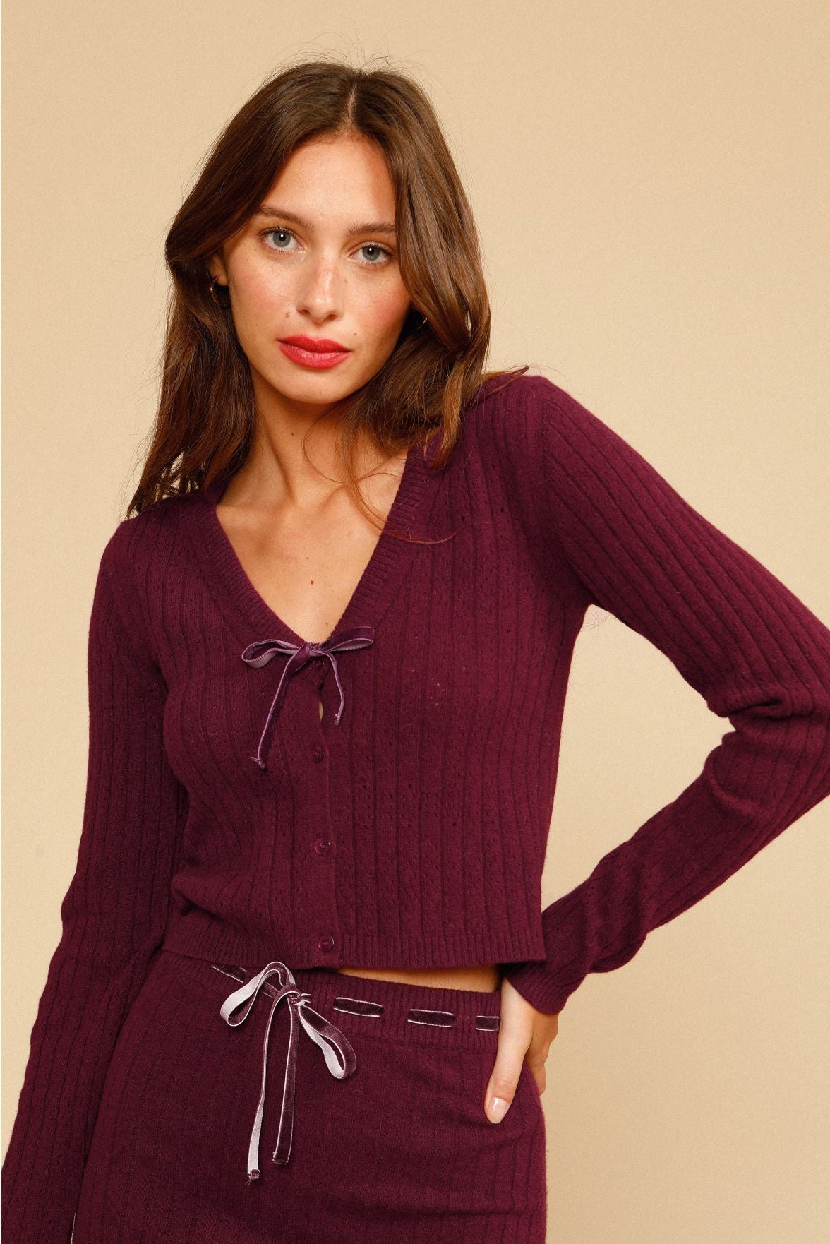 Indulge in luxury and comfort with our Ensemble Cirielle. This stylish two-piece set features a deep V rib long sleeve sweater and a midi ribbed knit skirt, both in a vintage burgundy color. The ribbed crop cardigan adds a sophisticated touch with a sexy V neckline and bow tie detail. Perfect for the upcoming seasons, complete the look with chunky boots and a classic baguette bag.