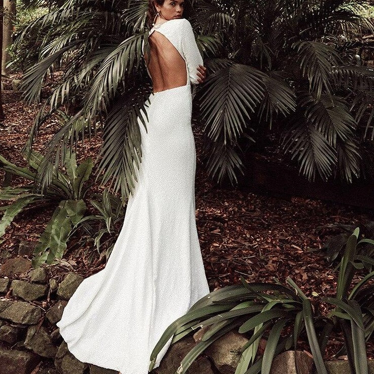 Introducing the Robe Sonyah, a luxurious and sophisticated white bridal dress. With a stunning open back, elegant long sleeves, and a flattering mermaid silhouette, this dress is the epitome of understated elegance. Perfect for the modern bride seeking a simple yet striking look on her special day.