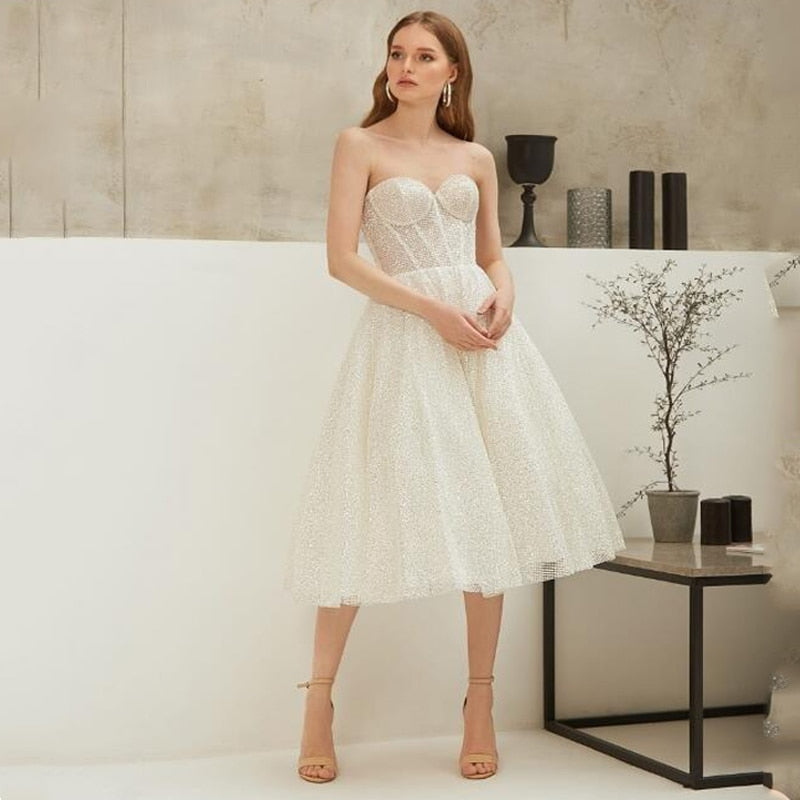 Indulge in the glamour of the Robe Blathnaid. This white vintage tea length cocktail dress is adorned with sparkling details, perfect for any special occasion. Embrace the timeless elegance of this exquisite piece, sure to turn heads and elevate your style.