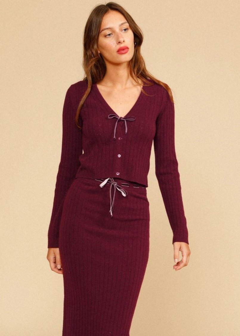 Indulge in luxury and comfort with our Ensemble Cirielle. This stylish two-piece set features a deep V rib long sleeve sweater and a midi ribbed knit skirt, both in a vintage burgundy color. The ribbed crop cardigan adds a sophisticated touch with a sexy V neckline and bow tie detail. Perfect for the upcoming seasons, complete the look with chunky boots and a classic baguette bag.