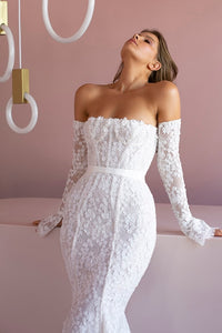 Indulge in the timeless elegance of the Robe Jeane. This strapless column showcases bare shoulders and long sleeves, adorned with delicate applique flowers. The exquisite lace flows into a dazzling train, while a white silk ribbon cinches the waist. Experience luxury with beaded accents and a delicate row of buttons down the back.