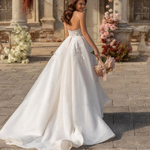 Indulge in luxury with the Robe Aneira. This deluxe, sleeveless wedding dress features a plunging v-neck and stunning appliques, invoking sensations of timeless elegance and sophistication. The open back adds a touch of sensuality, making it the perfect choice for the modern, stylish bride. Elevate your special day with this exquisite, high-end gown.