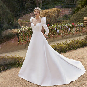 The Robe Cerys is a stunning satin wedding dress with a v-neckline, puffed sleeves, and a dramatic train. Designed for plus-size brides, it features elegant buttons and a flattering cut that will make you feel confident and beautiful on your special day. With a perfect balance of glamour and comfort, this dress is sure to make a lasting impression.