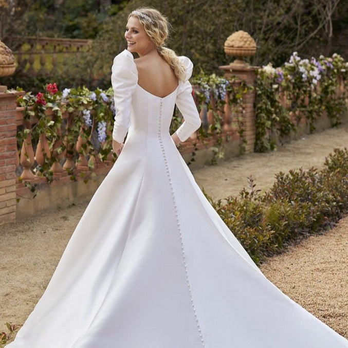 The Robe Cerys is a stunning satin wedding dress with a v-neckline, puffed sleeves, and a dramatic train. Designed for plus-size brides, it features elegant buttons and a flattering cut that will make you feel confident and beautiful on your special day. With a perfect balance of glamour and comfort, this dress is sure to make a lasting impression.