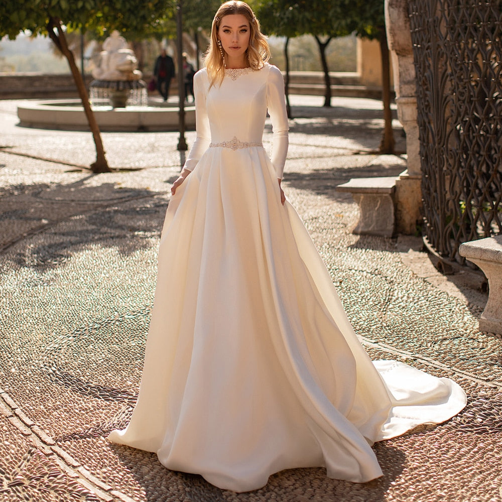 Wrap yourself in luxury with the Robe Mairead. Crafted with exquisite details, this custom satin robe features long sleeves and delicate pearl accents, perfect for any modest bride. Feel elegant and exclusive on your special day. Available in a variety of sizes to ensure the perfect fit.