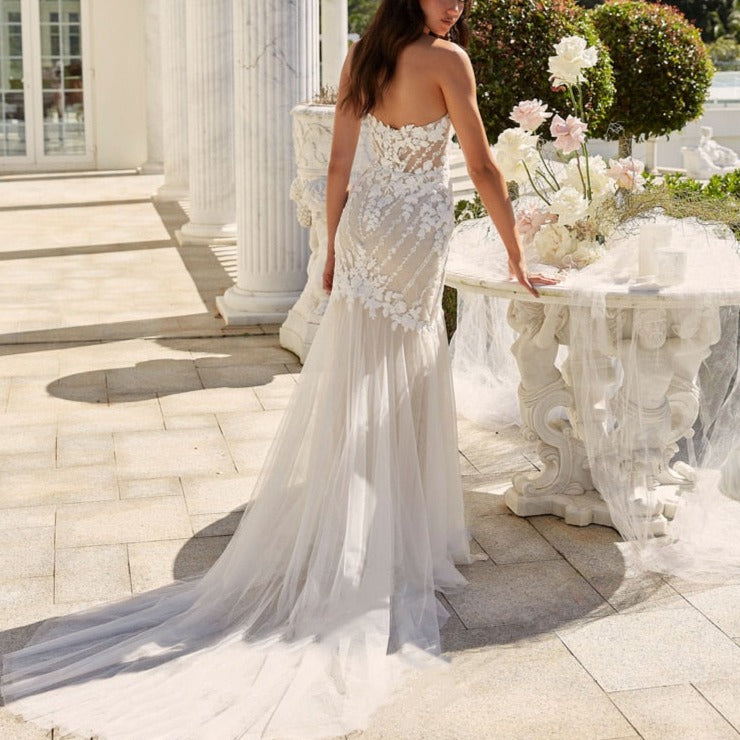 Step into elegance with the Robe Nerissa. This stunning trumpet style wedding dress features a unique off-the-shoulder design, complete with delicate appliques and a graceful open back. With a floor-length hem, this dress is perfect for any special occasion.