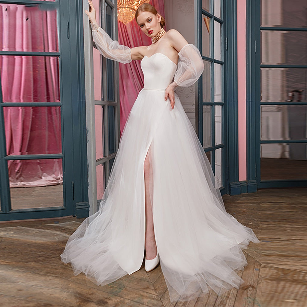 Be the belle of the ball (or wedding) in our stunning Robe Zari! This elegant and versatile gown features a removable puffy sleeve, side slit, and unique tulle design. Perfect for any special occasion, this dress won't disappoint. 