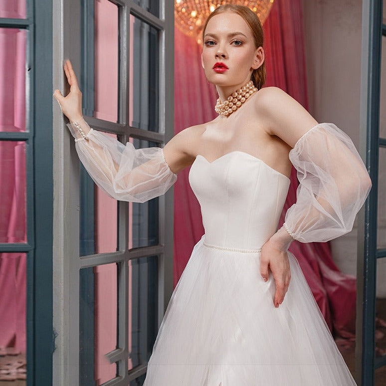 Be the belle of the ball (or wedding) in our stunning Robe Zari! This elegant and versatile gown features a removable puffy sleeve, side slit, and unique tulle design. Perfect for any special occasion, this dress won't disappoint. 