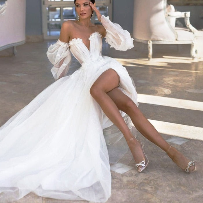 Designed for a princess bride, the Robe Araminta is a stunning white tulle dress with billowing puff sleeves and a seductive high leg slit. Its intricate appliques and sweetheart neckline add a touch of elegance to this sexy and modern design. Perfect for making a statement on your big day.