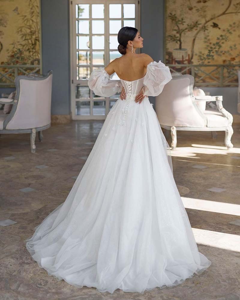 Designed for a princess bride, the Robe Araminta is a stunning white tulle dress with billowing puff sleeves and a seductive high leg slit. Its intricate appliques and sweetheart neckline add a touch of elegance to this sexy and modern design. Perfect for making a statement on your big day.